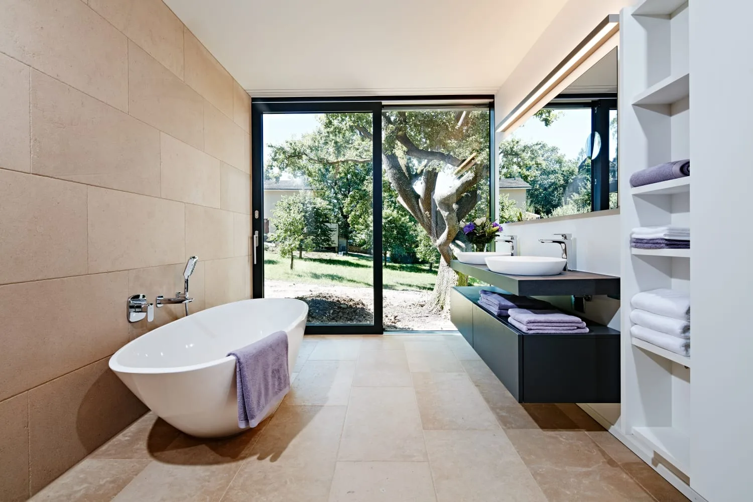 Badezimmer mit großformatigen hellen Natursteinplatten an Wand und Boden und freistehender Wanne